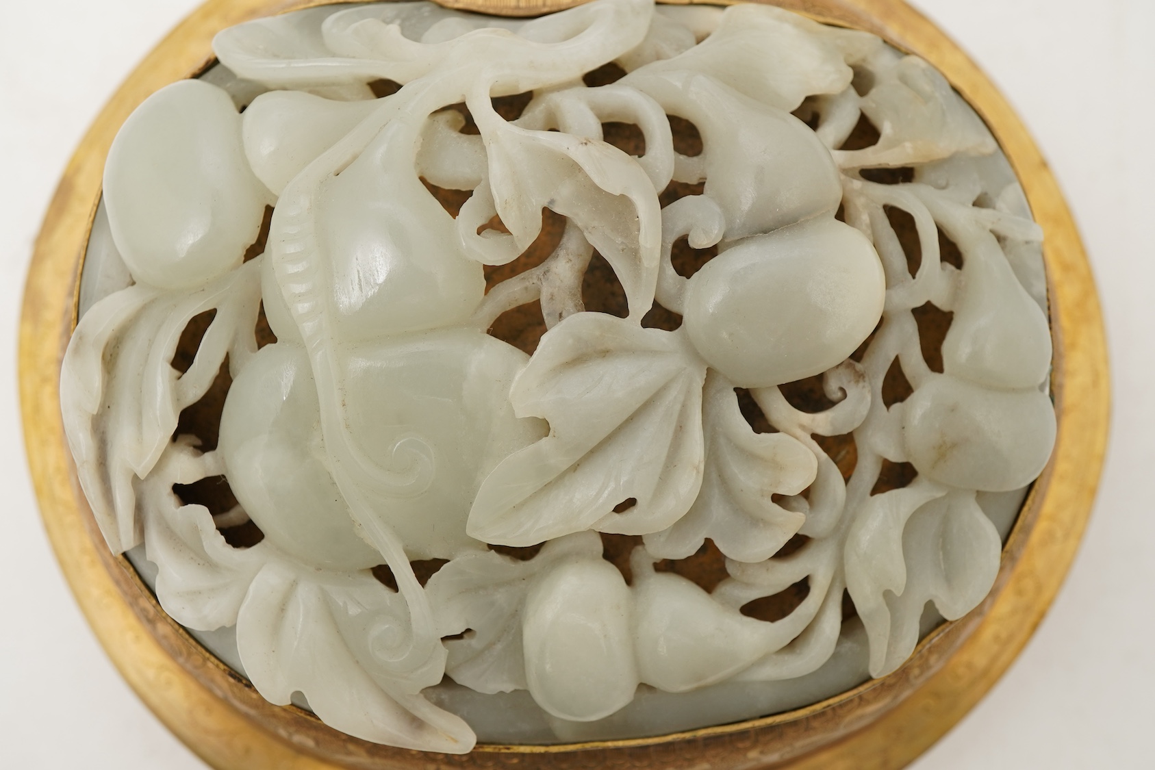 A Chinese pale celadon jade oval plaque, 17th/18th century, mounted on a late Qing gilt copper jar